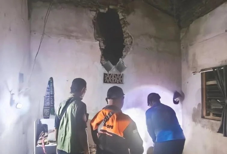 Petugas BPBD Situbondo mengevakuasi pohon kelapa tumbang yang merusak rumah warga di Banyuputih.