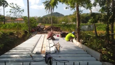 Babinsa Sertu Dadang gotong royong bersama warga Lebeng Barat merakit besi jembatan
